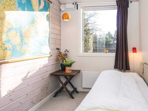 A room with a bed, a map on the wall, a small table with a plant, and a window with curtains. - 4 Star Holiday Home in Ans By (Ans)