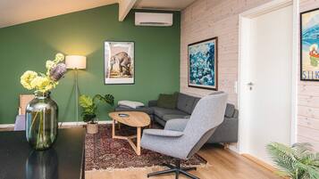 Una sala de estar con sofá, sillón, mesa de centro y un jarrón con flores.