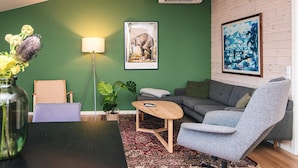 A modern living room with a green wall, a grey sofa, a blue armchair, a wooden coffee table, and a floor lamp. - 4 Star Holiday Home in Ans By (Ans)
