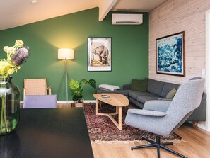Una sala de estar moderna con una pared verde, un sofá gris, un sillón azul, una mesa de centro de madera y una lámpara de pie.