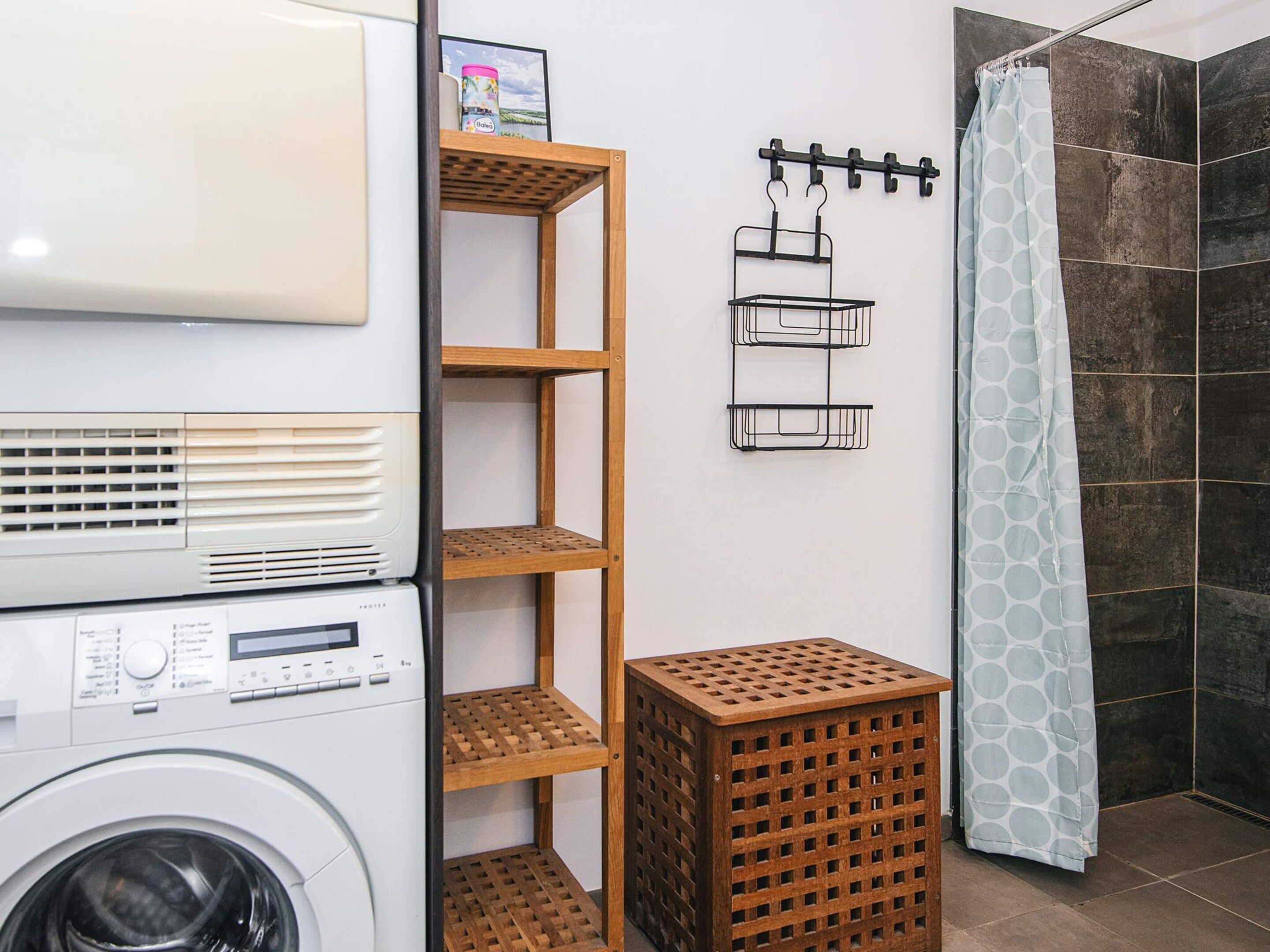 A laundry area with stacked dryers, wooden shelves, and a shower curtain.