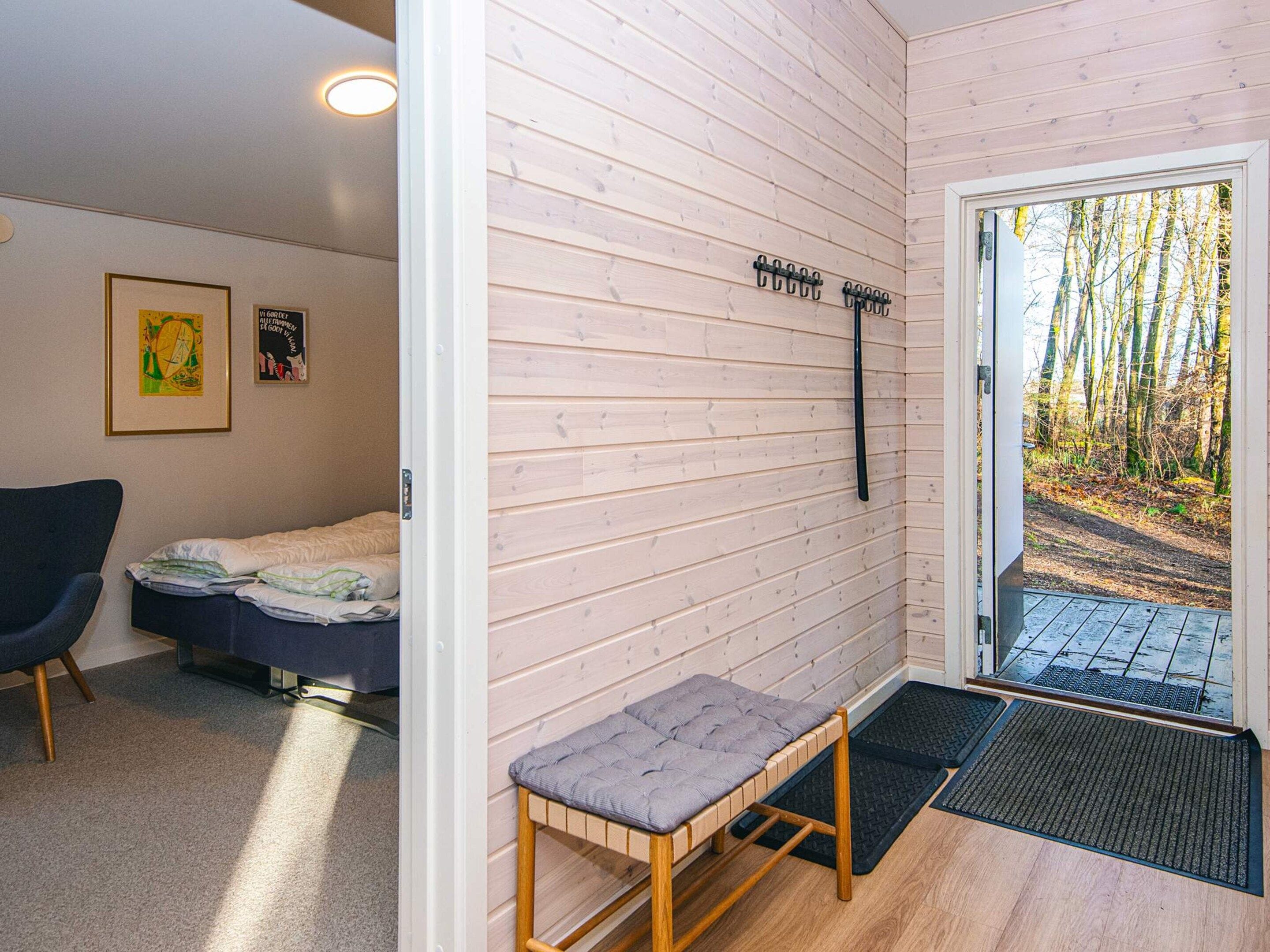 A room with a bed, a bench, a chair, and a door leading to an outdoor area with a view of trees.