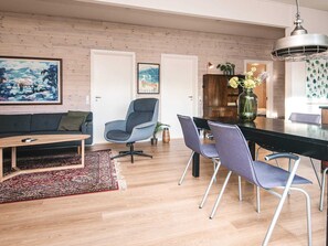 Ein modernes Wohnzimmer mit einer Couch, einem Esstisch mit Stühlen, einem Couchtisch, einem Teppich und einem Bild an der Wand.