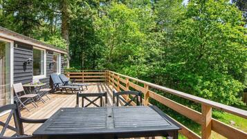 A wooden deck with outdoor furniture, surrounded by dense trees.