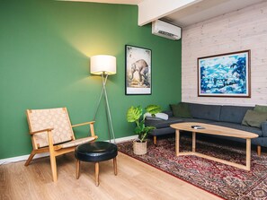 A modern living room with a green wall, a grey sofa, a wooden coffee table, a floor lamp, and a framed painting. - 4 Star Holiday Home in Ans By (Ans)
