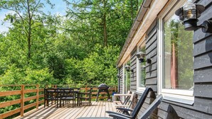 A wooden deck with outdoor furniture, including chairs and a table, overlooking a forested area. - 4 Star Holiday Home in Ans By (Ans)