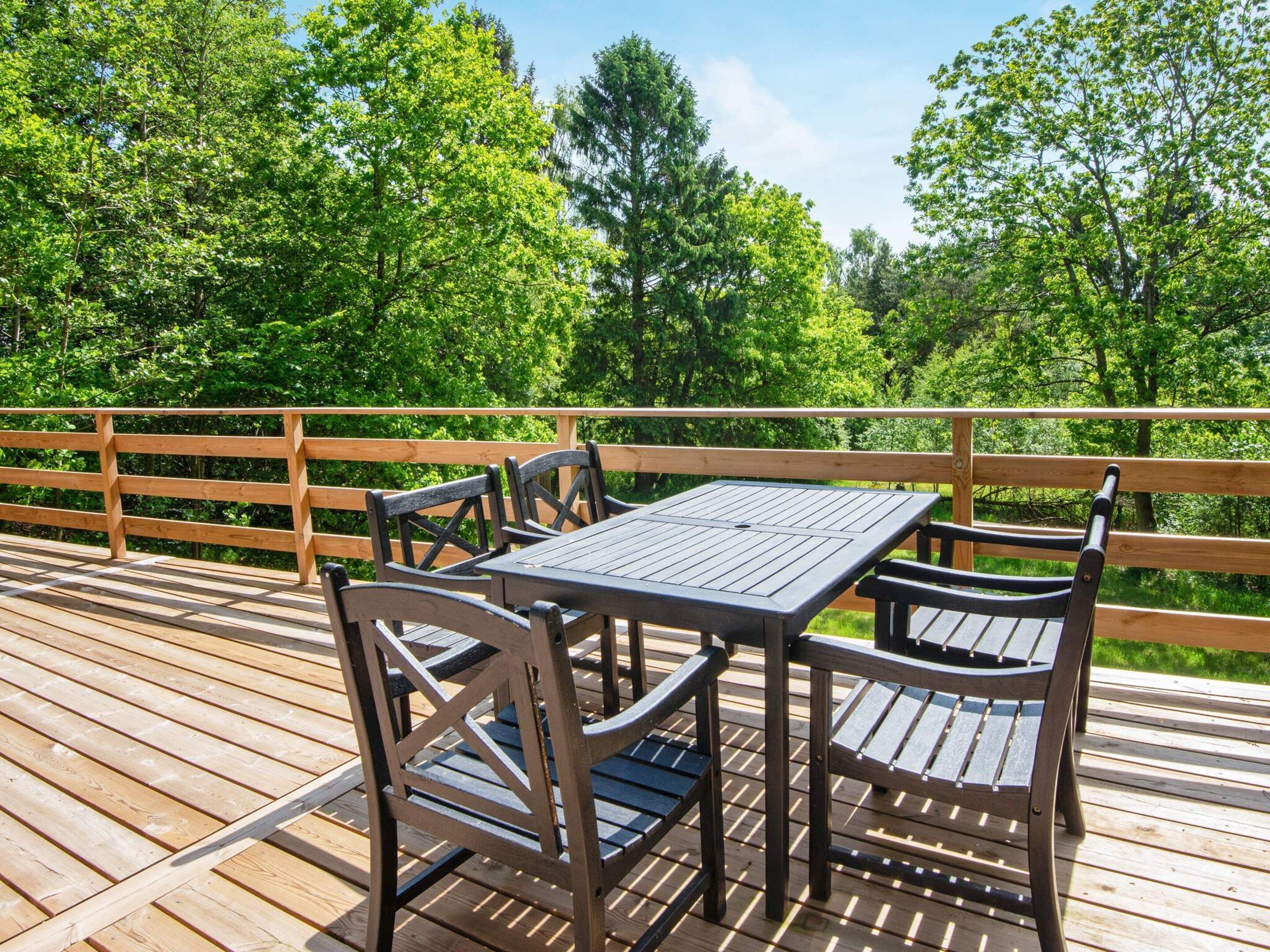A wooden deck with a table and chairs, surrounded by a wooden railing, overlooking a forested area.