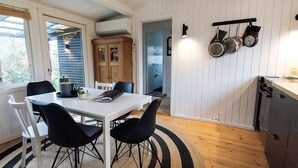 A dining area with a white table and black chairs, a kitchen with wooden cabinets and hanging pots, and a view through a door to a blue room. - 6 Person Holiday Home in Jaegerspris-by Traum (Jægerspris)
