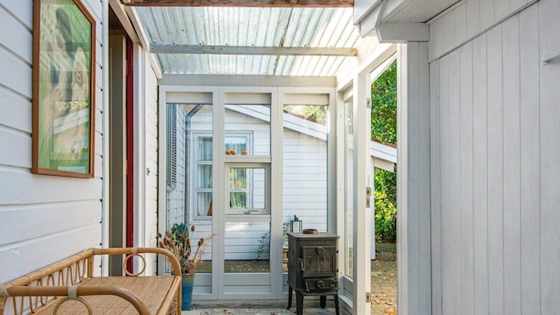 A covered porch with a wicker chair, a small table, and a vintage stove.