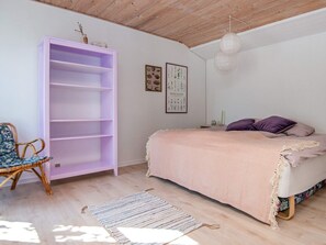 Un dormitorio con una cama, una estantería morada, una silla de mimbre, una alfombra y una lámpara en el techo.