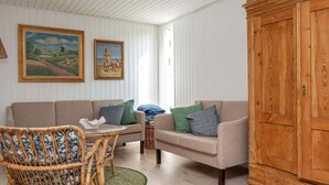 A cozy living room with a sofa, a wicker chair, a wooden cabinet, and two framed paintings on the wall.