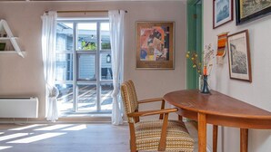 A room with a wooden ceiling, a dining table with chairs, a window with curtains, and framed artwork on the walls.