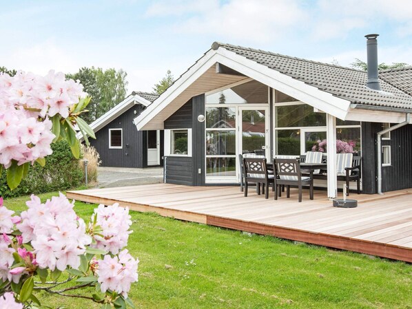 A modern house with a covered patio, a wooden deck, and a garden with pink flowers. - 8 Person Holiday Home in Vaeggerlose-by Traum (Vaeggerlose)