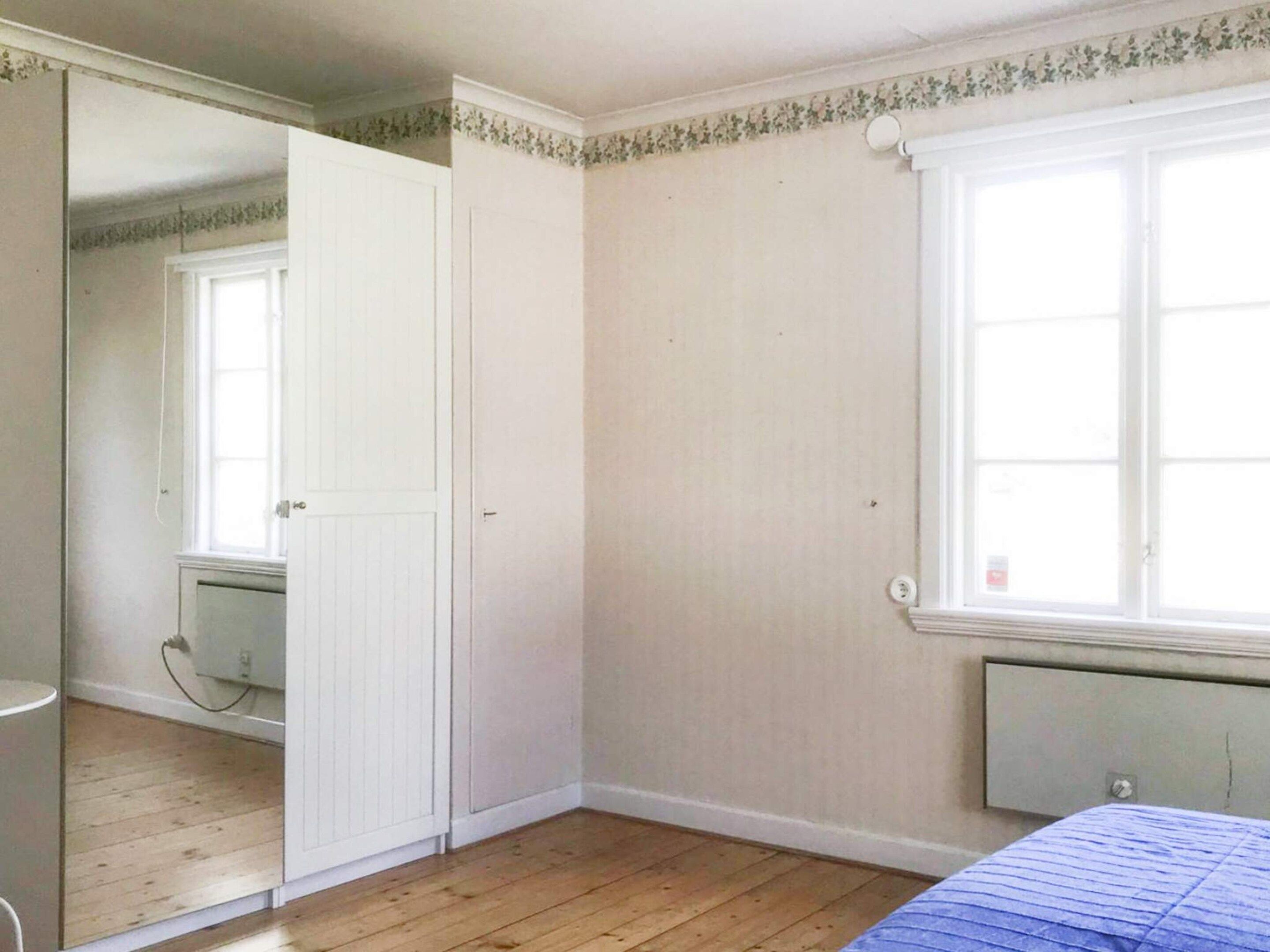 A bedroom with a wooden floor, a radiator, a window, and a door.