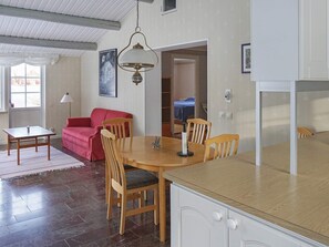 Un coin repas comprenant une table ronde en bois, quatre chaises, un canapé rouge et une suspension.