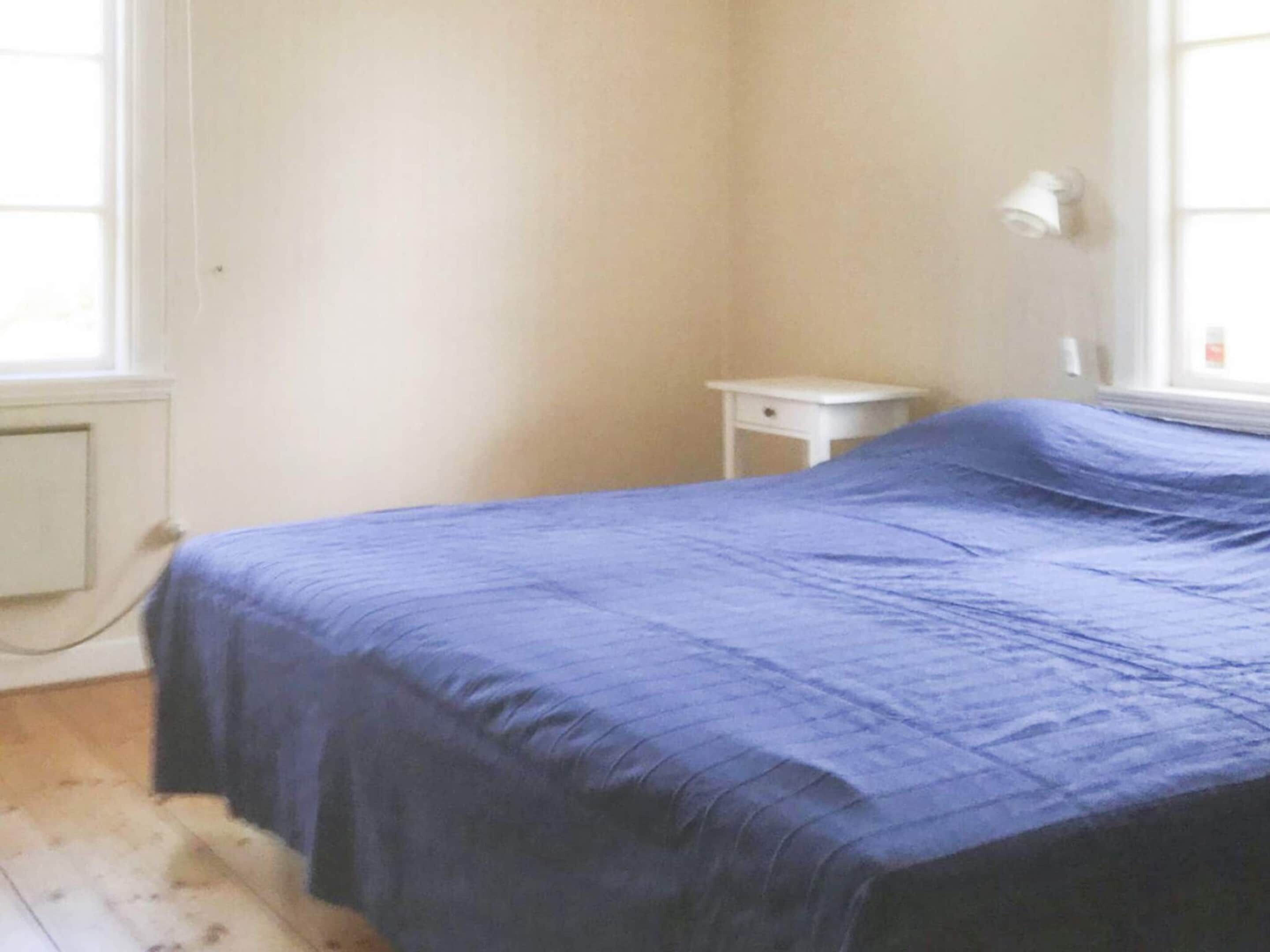 A room with a bed, a small white nightstand, and a window.
