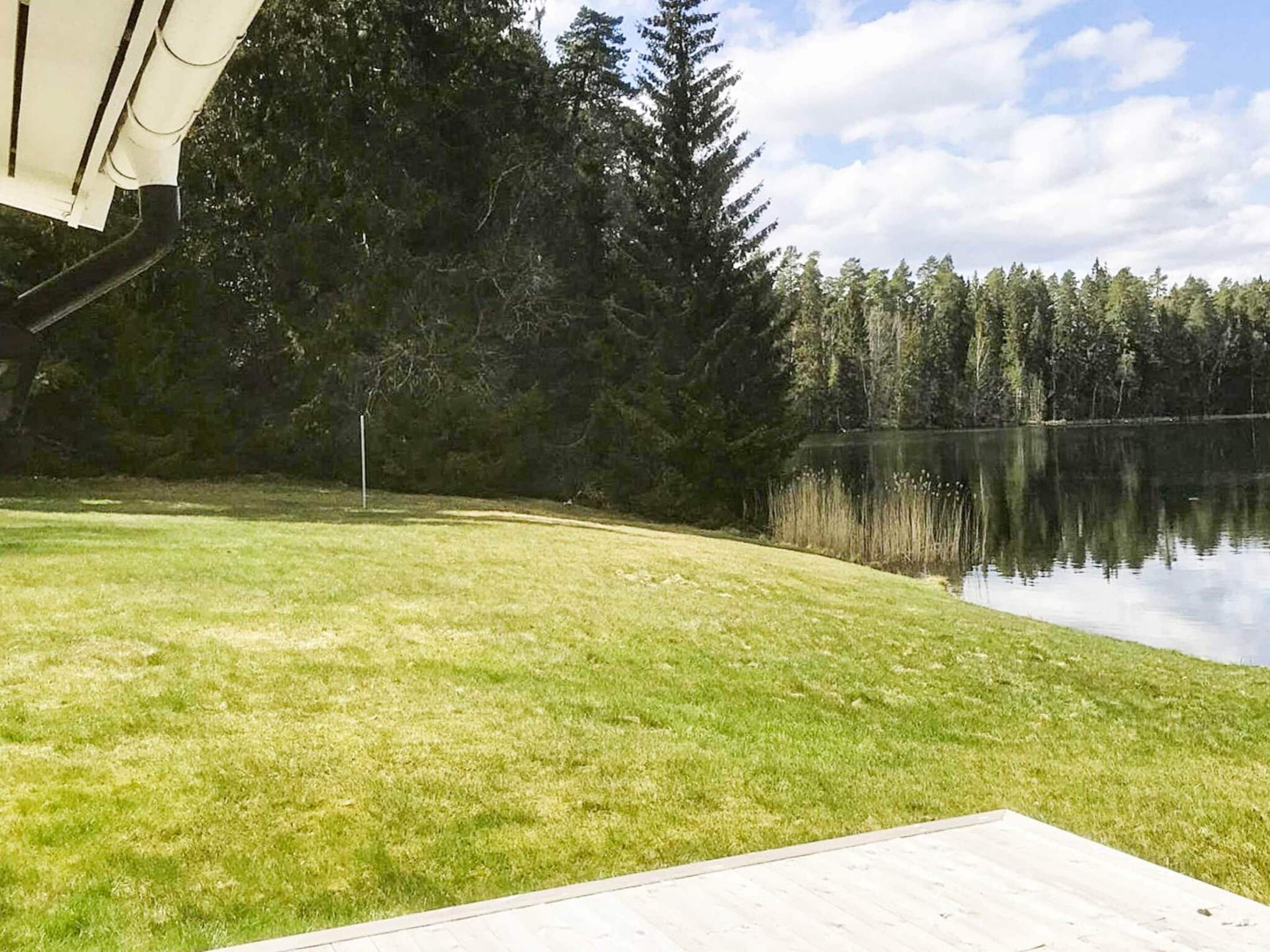 A grassy area with a wooden deck and a lake surrounded by trees.