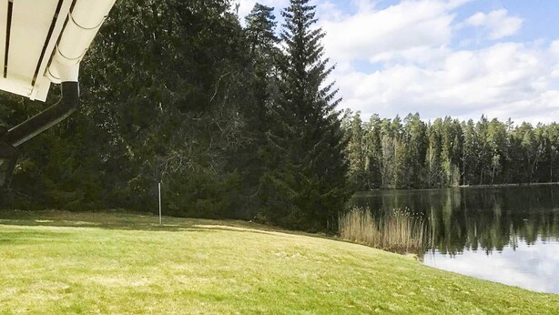 A grassy area with a wooden deck and a lake surrounded by trees. - 5 Star Holiday Home in Asbro (Asbro)