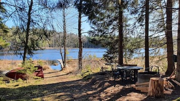A campsite with a table and chairs, a red canoe, and a wooden deck overlooking a lake.