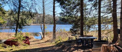 Un terrain de camping équipé d’une table et de chaises, d’un canoë rouge et d’une terrasse en bois donnant sur un lac.