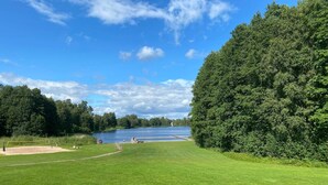 Une zone herbeuse avec un lac, des arbres et un ciel dégagé.