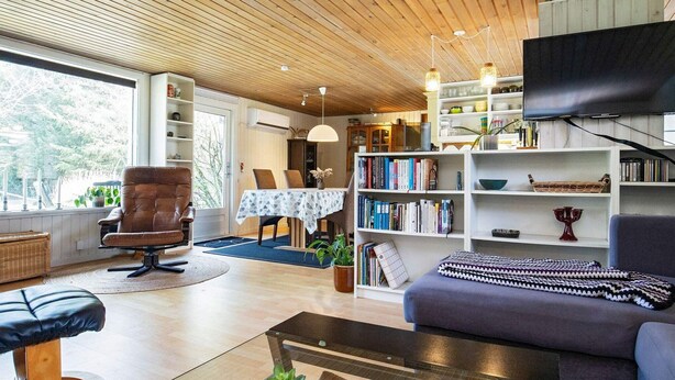 A modern living room with a sofa, a coffee table, a bookshelf, and a dining area with a table and chairs. - 8 Person Holiday Home in Hurup Thy-by Traum (Hurup Thy)