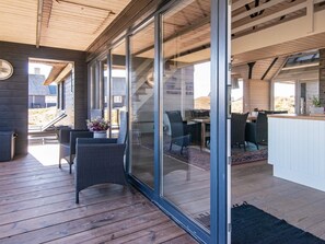 A modern interior with a wooden deck, glass sliding doors, and a dining area with wicker furniture.