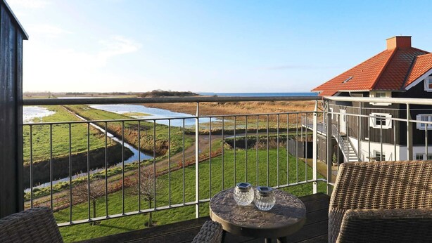 A balcony with wicker furniture, a small table with two salt shakers, and a view of a river and fields. - 6 Person Holiday Home in Bogense (Bogense)