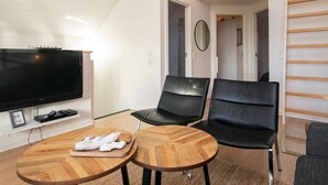 A modern living room with a flat-screen TV, two black leather chairs, a wooden coffee table, and a woven light fixture. - 6 Person Holiday Home in Bogense (Bogense)