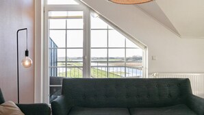 A modern living room with a large window, a dark green sofa, a round coffee table, and a hanging light fixture. - 6 Person Holiday Home in Bogense (Bogense)