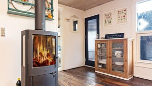 Een kamer met een houtkachel, houten vloeren, een kast met glazen deuren en een deur met een geëtste glazen ruit.