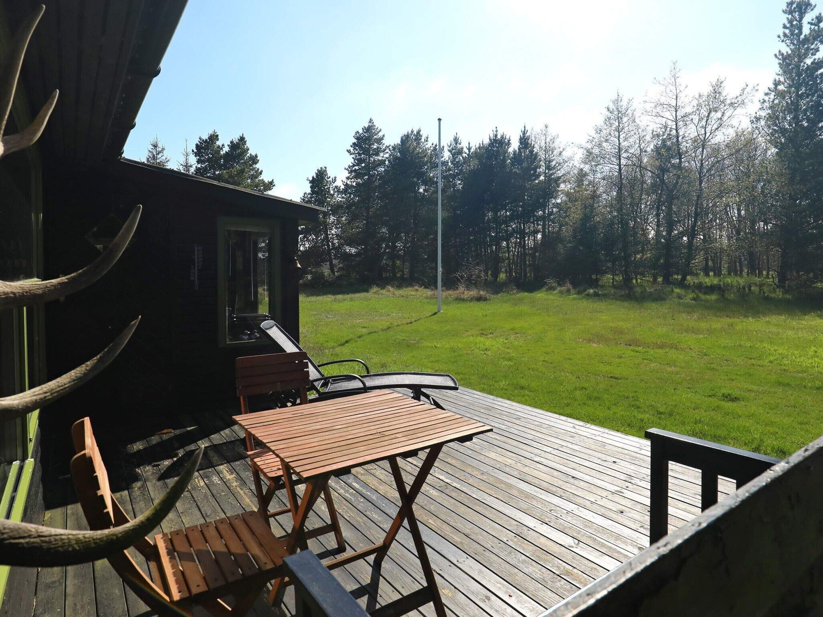 Un terrazzo in legno con tavolo e sedie, affacciato su una zona erbosa con alberi.