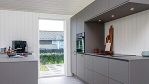 Ett modernt kök med gråa skåp, en stor köksö och utsikt över ett hus genom en skjutdörr.