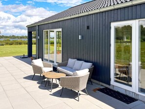 A modern building with a grey exterior, large sliding glass doors, and outdoor seating with wicker furniture. - Stylish Lakeview Retreat-by Traum (Ansager)