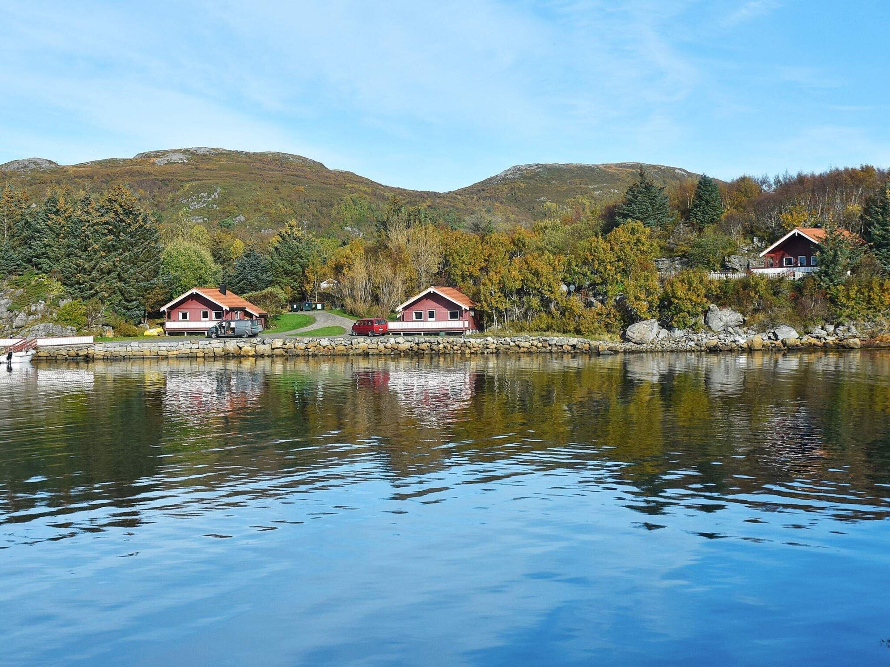 Ein Seeblick mit zwei Häusern mit roten Dächern, einer Steinmauer und herbstlich gefärbten Bäumen.