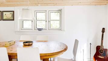 A dining area with a round wooden table, white chairs, a hanging lamp, and a guitar against the wall.