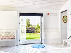 A room with a white bench, a blue rug, and a door leading to a garden.