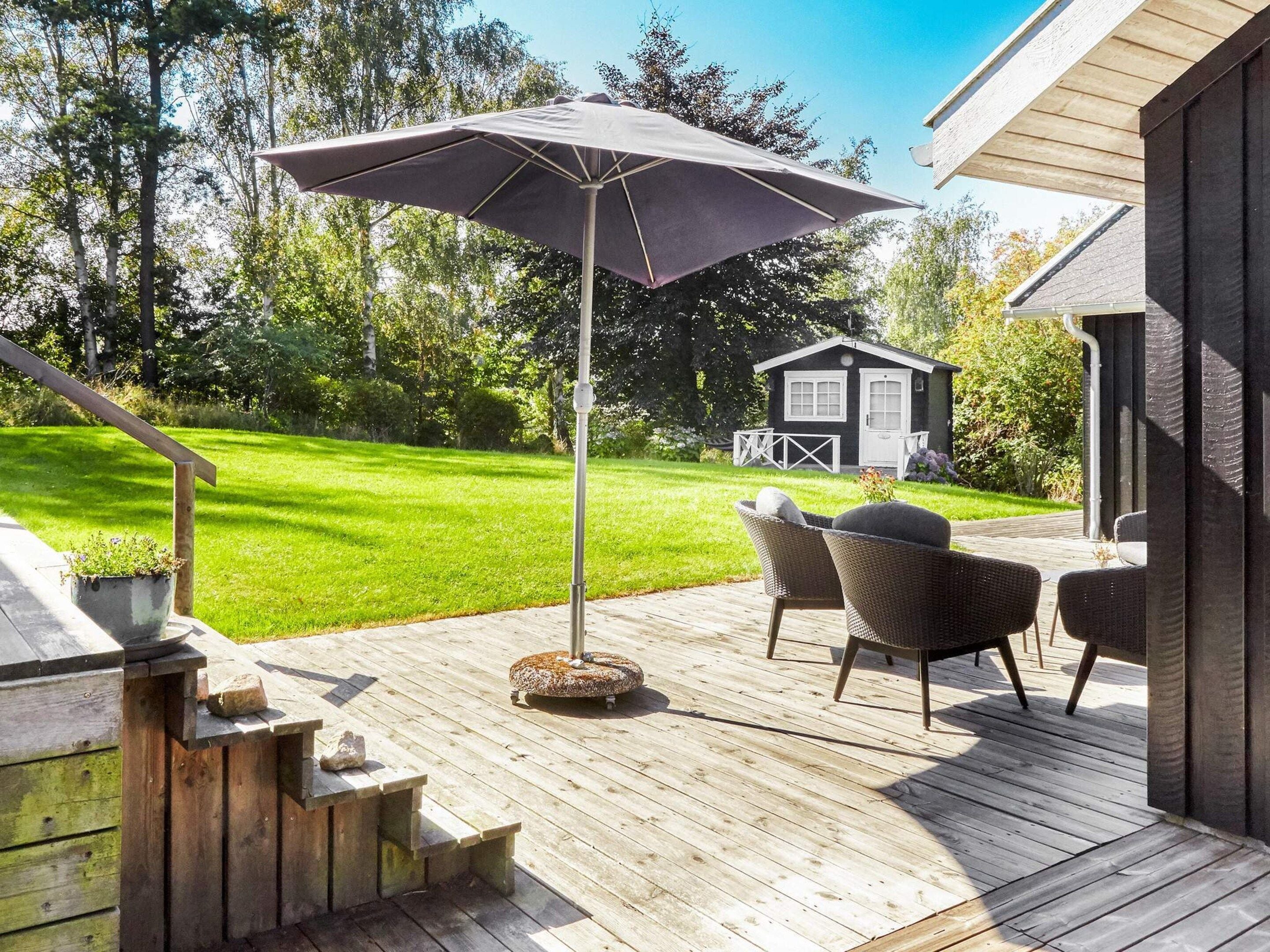 A wooden deck with outdoor furniture, a patio umbrella, and a small shed in the background.