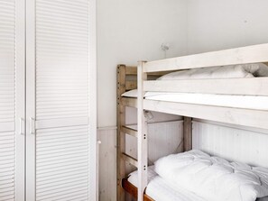 Una cama litera con ropa blanca en una habitación con paredes y puerta blancas.