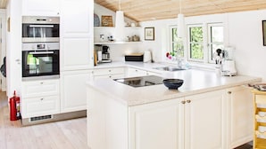 A modern kitchen with white cabinetry, a central island, a built-in oven, and a coffee station. - 4 Star Holiday Home in Nykobing Sj (Nykobing Sjaelland)