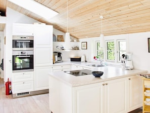 A modern kitchen with white cabinetry, a central island, a built-in oven, and a coffee station. - 4 Star Holiday Home in Nykobing Sj (Nykobing Sjaelland)