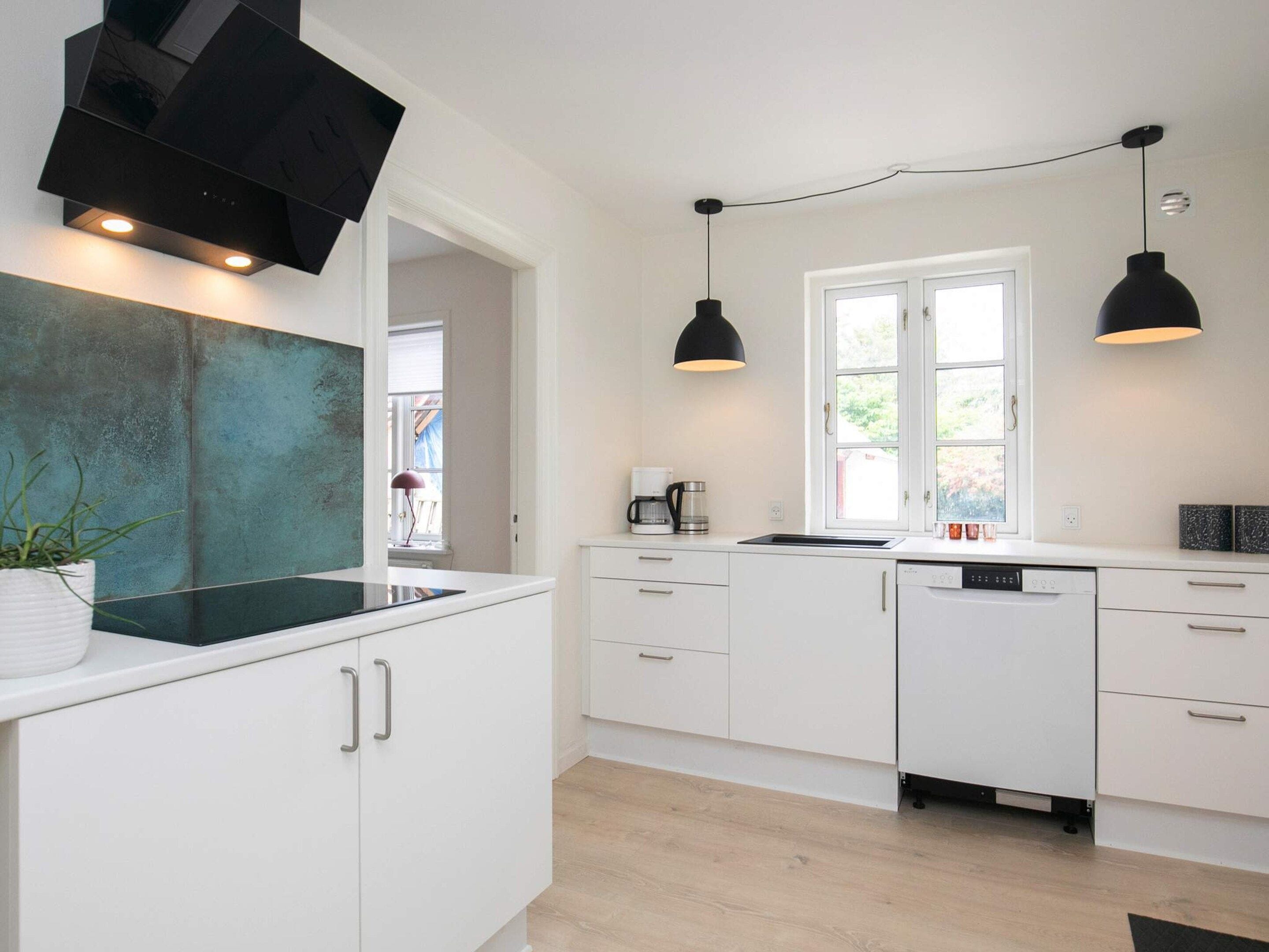 Une cuisine moderne avec des meubles blancs, un plan de travail noir et des luminaires suspendus.