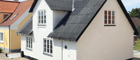 Ein weißes, zweistöckiges Haus mit einem steilen Satteldach, einer kleinen Veranda und einer sichtbaren Haustür.