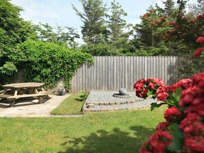Un jardin avec une clôture en bois, un abreuvoir à oiseaux en pierre et une table de pique-nique.