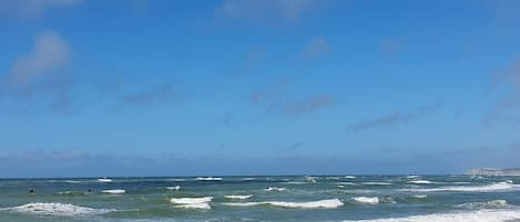 Una playa con olas, cielo despejado y un paseo marítimo de madera.