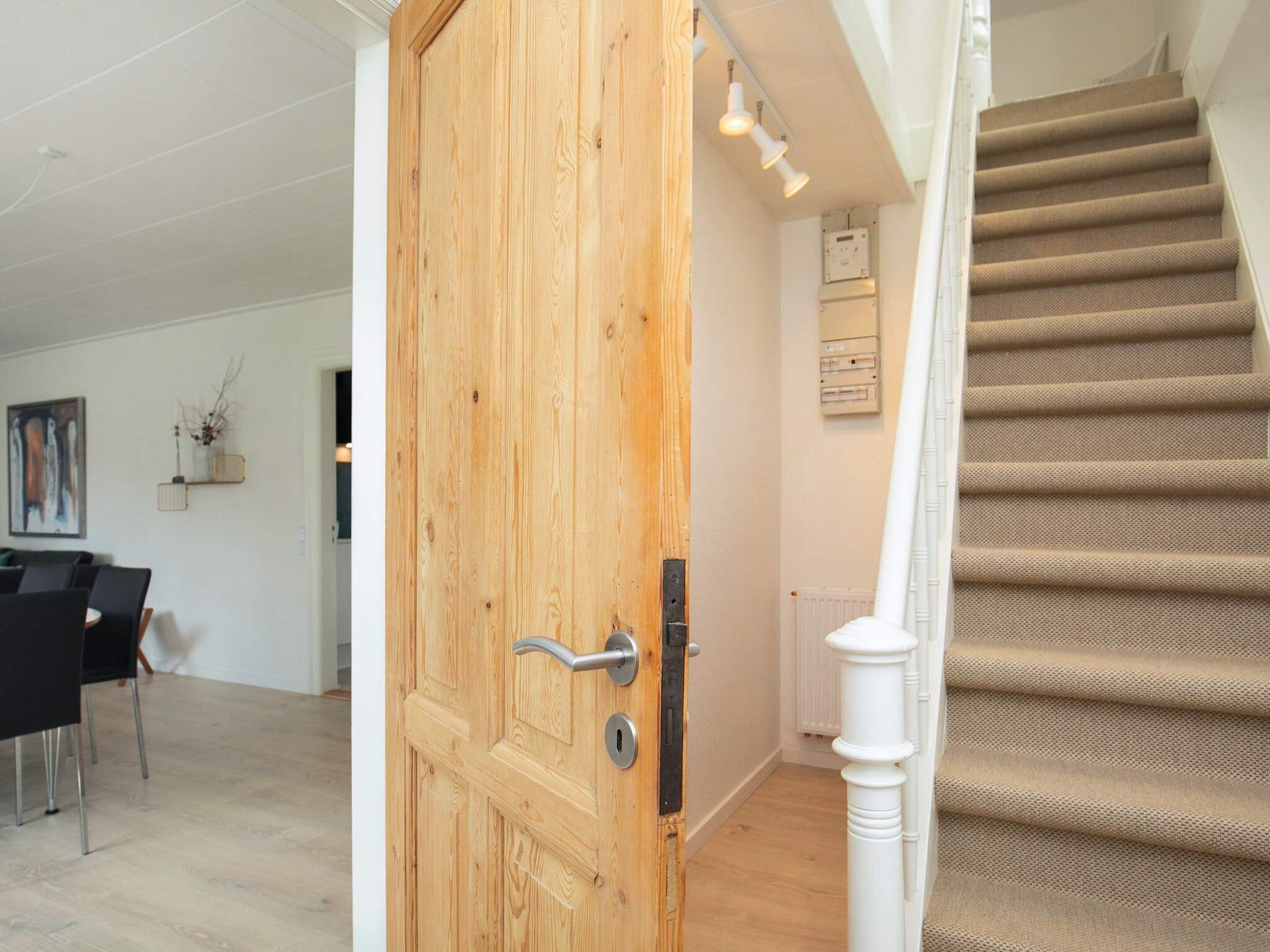 A wooden door with a modern handle, a staircase with beige carpet, and a white radiator on the wall.