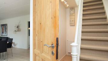 Uma porta de madeira com puxador moderno, escada com carpete bege e um radiador branco na parede.