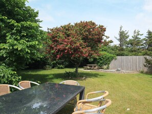Un jardin avec une table de pique-nique, des chaises en osier, un arbre aux fleurs rouges et une clôture en bois.