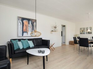 Una sala moderna con un sofá de cuero negro, una mesa de centro blanca y un comedor con una mesa y sillas negras.