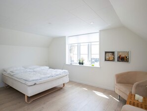 Une chambre à coucher avec un lit, une fenêtre, une chaise et deux tableaux accrochés au mur.